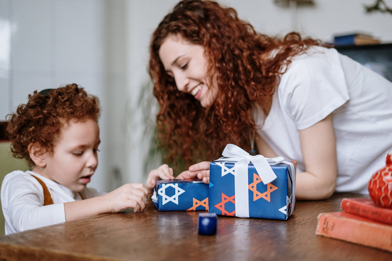 A joyful moment of a mother and son wrapping a Hanukkah gift together indoors.